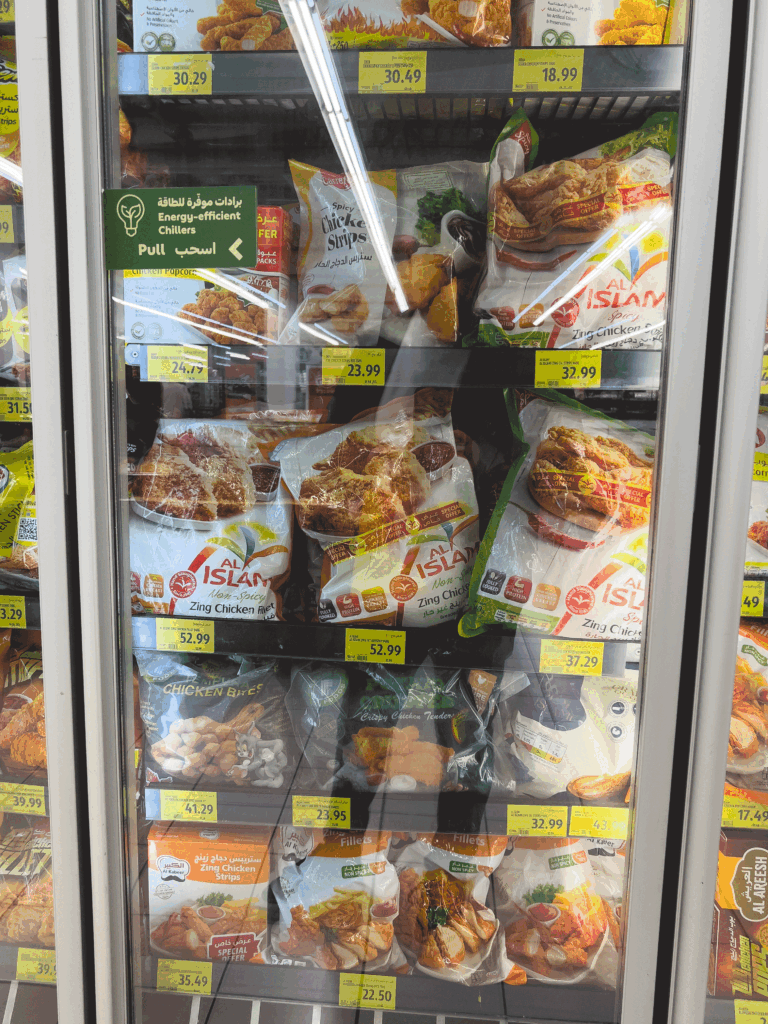 Frozen poultry products on shelves in a Dubai supermarket, featuring Al Islami and Carrefour private label items.