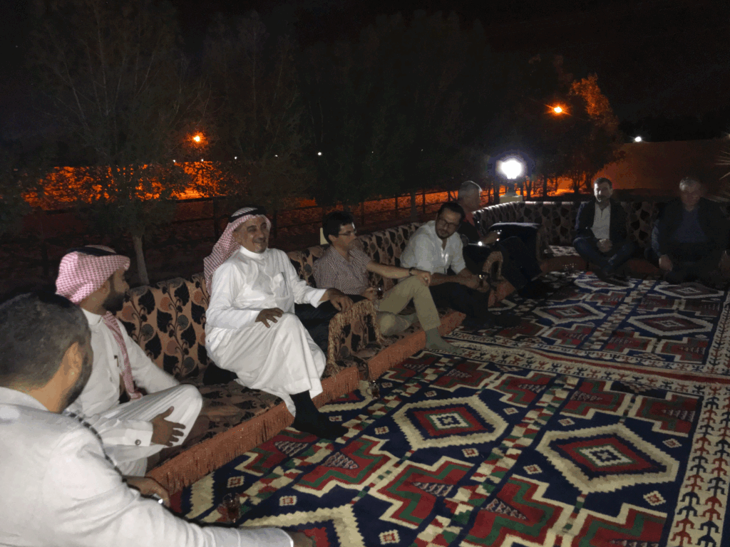 Traditional evening gathering in Saudi Arabia with local hosts and international guests seated outdoors in a majlis setting.