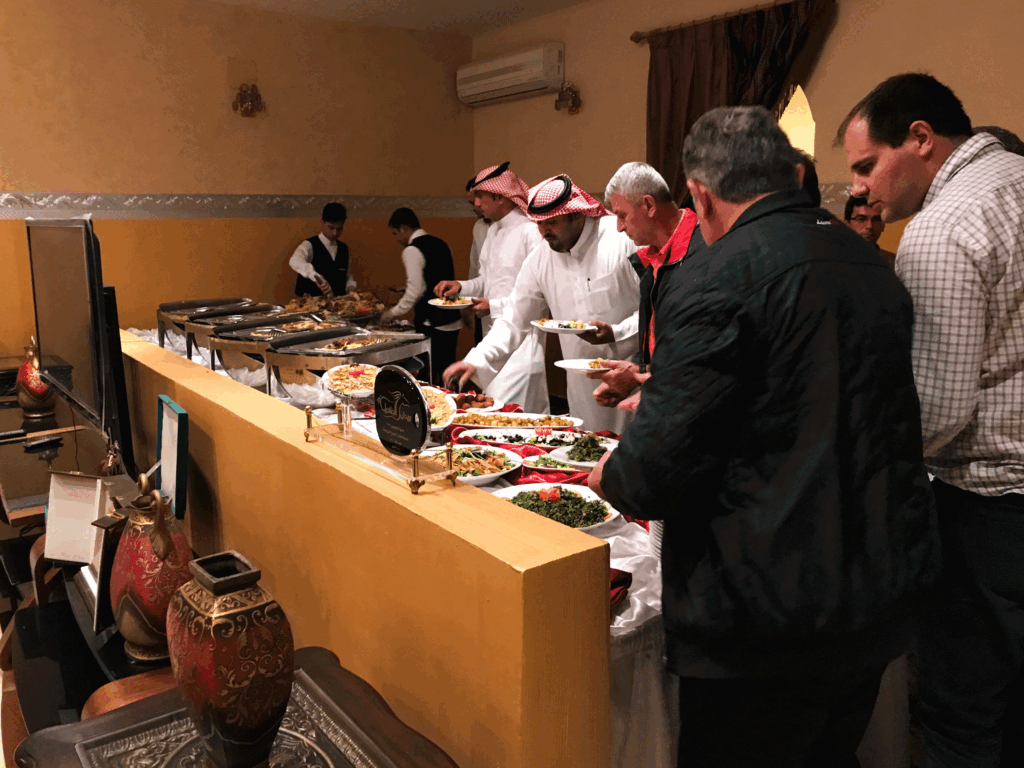 Buffet style dinner during a hospitality gathering in Saudi Arabia, with guests and hosts serving traditional dishes.