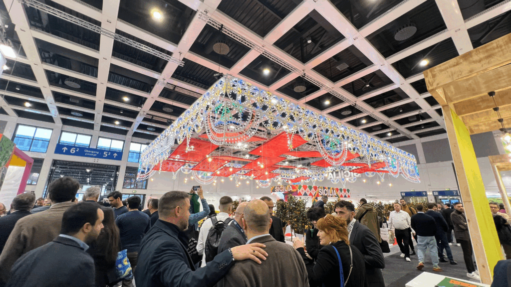 Crowded Sicilian pavilion at Fruit Logistica, with traditional decorative lights and high visitor activity.