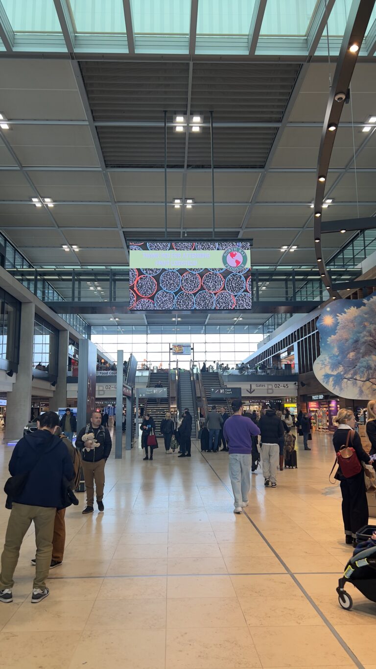 Entrance hall at Messe Berlin during Fruit Logistica, showing visitors walking towards the central escalators.